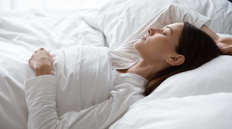 Femme dormant paisiblement dans un lit, symbolisant l'importance du sommeil pour la régénération de la peau, complétée par les soins visage bio de IUM Paris.