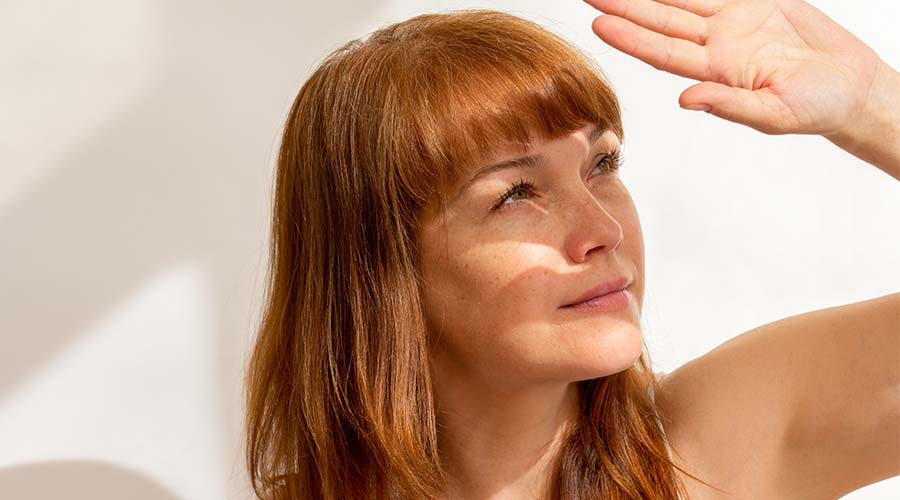 Femme rousse à la peau lumineuse se protégeant du soleil, préparée grâce à une routine visage bio naturelle aux oligo-éléments.