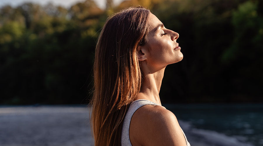 Femme au naturel profitant du soleil printanier, peau lumineuse et saine grâce à une routine de soins visage bio enrichis en oligo-éléments.