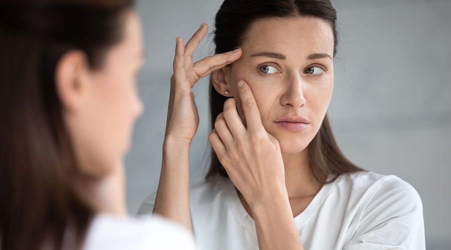 Femme examinant des ridules sur son visage dans un miroir, illustrant les effets de la déshydratation de la peau et la nécessité de soins visage hydratants et revitalisants comme ceux de IUM Paris.