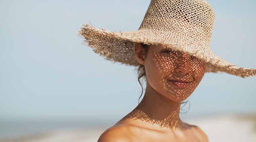 Femme portant un chapeau de paille sur la plage, illustrant l'effet protecteur et nourrissant des soins visage bio et naturels de IUM Paris sous le soleil.
