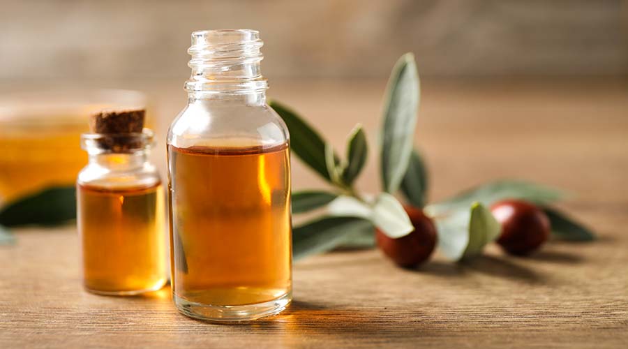 Deux flacons d'huile de jojoba de face sur une table avec fruits du jojoba