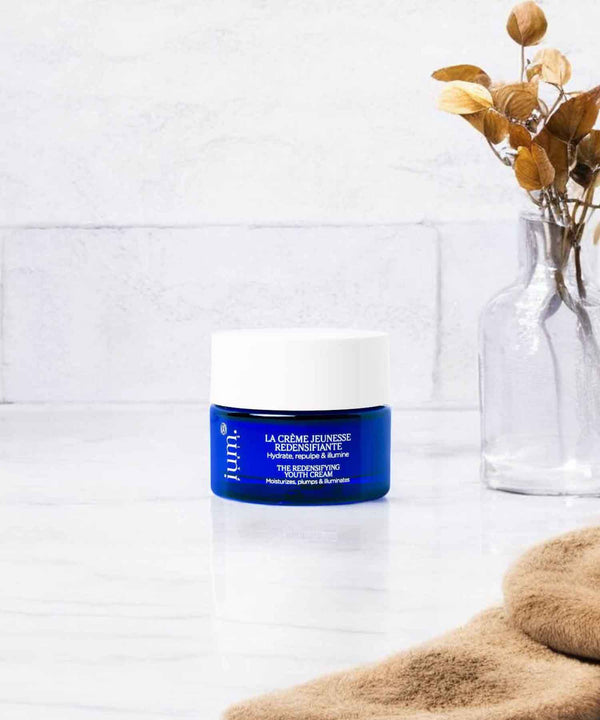 Pot de Crème Jeunesse Redensifiante IUM Paris posé sur une surface de salle de bain avec des éléments naturels en arrière-plan, soin visage hydratant et repulpant, certifié bio.