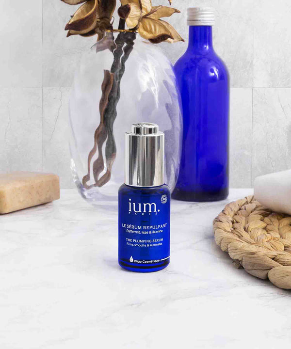 serum bio visage flacon bleu de serum ium dans salle de bain lumineuse avec accessoires de couleur beige