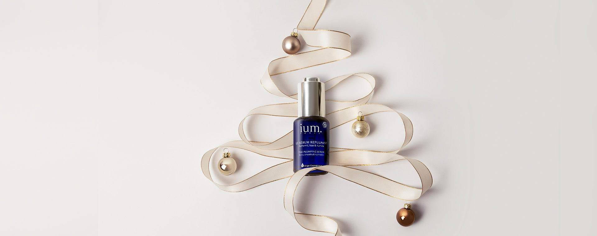 Sérum Repulpant IUM Paris présenté en décoration de Noël avec un ruban en forme de sapin et des ornements dorés, idéal pour offrir un soin bio et naturel.