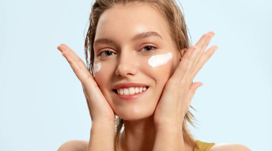 Femme souriante appliquant une crème visage IUM bio et naturelle, soin hydratant à base d’oligo-éléments.