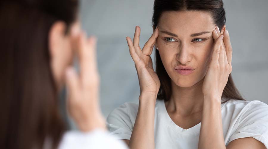 Femme observant ses premières rides dans le miroir, illustrant l'importance des soins anti-âge naturels et bio pour une peau lisse et éclatante.  