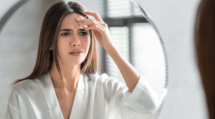 Jeune femme inquiète devant son miroir en observant des signes de rides et de perte de fermeté, mettant en avant l'importance des soins visage naturels et bio.