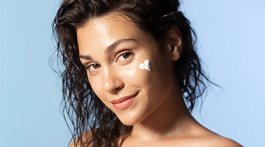 Femme au teint lumineux appliquant une crème hydratante sur son visage, illustrant le rituel sérum + crème pour restaurer éclat et équilibre de la peau à la rentrée