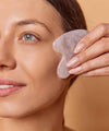 woman in front massages her face with a Gua Sha Rose Quartz IUM stone