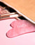 Pierre de massage Gua Sha en Quartz rose dépasse d'une trousse de maquillage